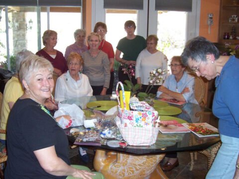 A group of elderly women gathered around a dining table adorned with crafting supplies, smiling and engaging in a craft activity.